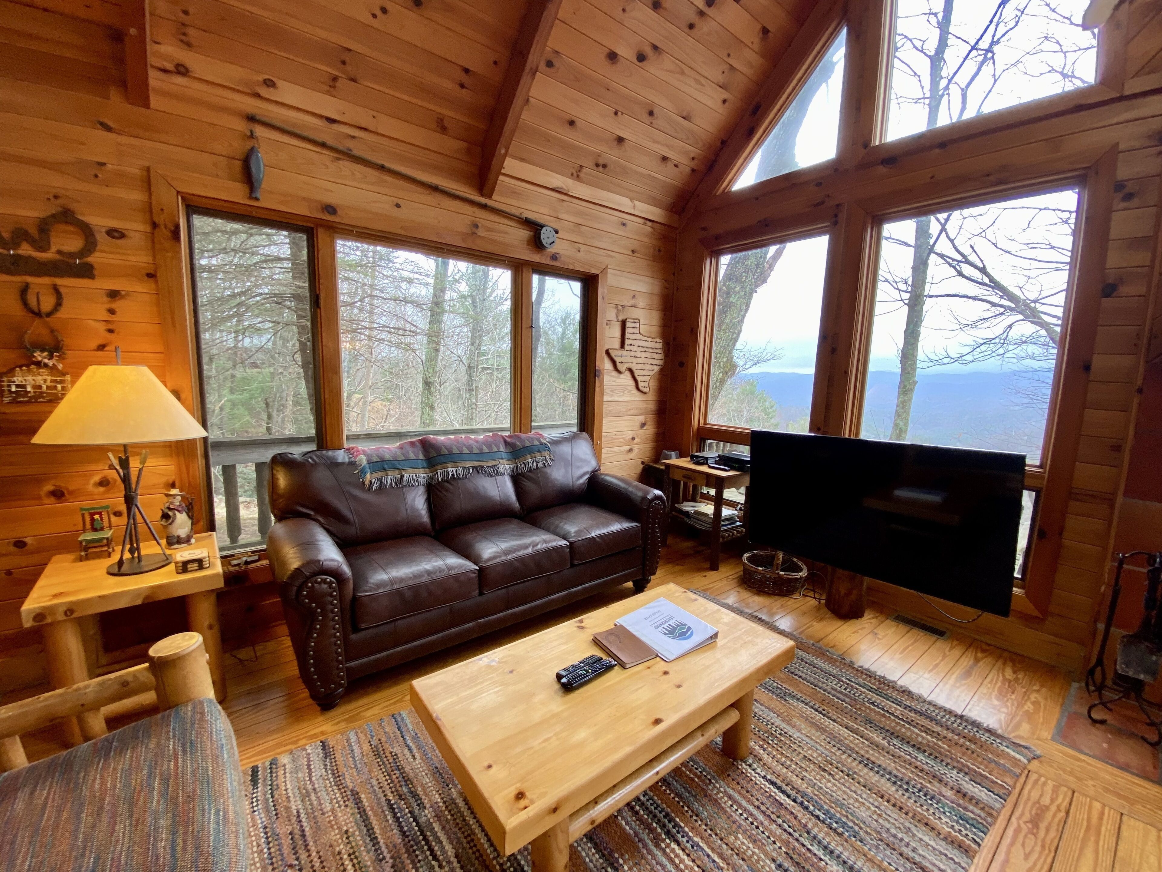 L’intérieur de ce chalet confortable est doté d’un canapé en cuir, d’une table basse en bois et d’un téléviseur. De grandes fenêtres offrent une vue sur la forêt environnante.
