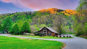 A rustic cabin with a large porch, surrounded by lush green fields and a forested hill in the background. - Pet-Friendly,Cozy Cabin,Hot Tub,Wood Fireplace,WiFi (Ferguson)