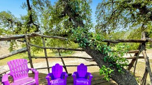 A wooden deck with three purple Adirondack chairs and a large tree trunk. - Blissful RV Retreat in Canyon Lake! Only 5 minutes from the lake and river! (Canyon Lake)