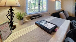 A neatly arranged room with a bed, a bedside lamp, a potted plant, a window with blinds, and a sign on the windowsill. - Blissful RV Retreat in Canyon Lake! Only 5 minutes from the lake and river! (Canyon Lake)