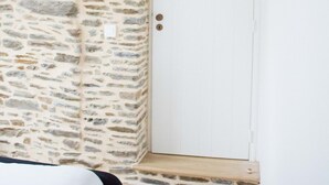 Una stanza con una parete in pietra, una porta bianca e un letto con copriletto bianco.