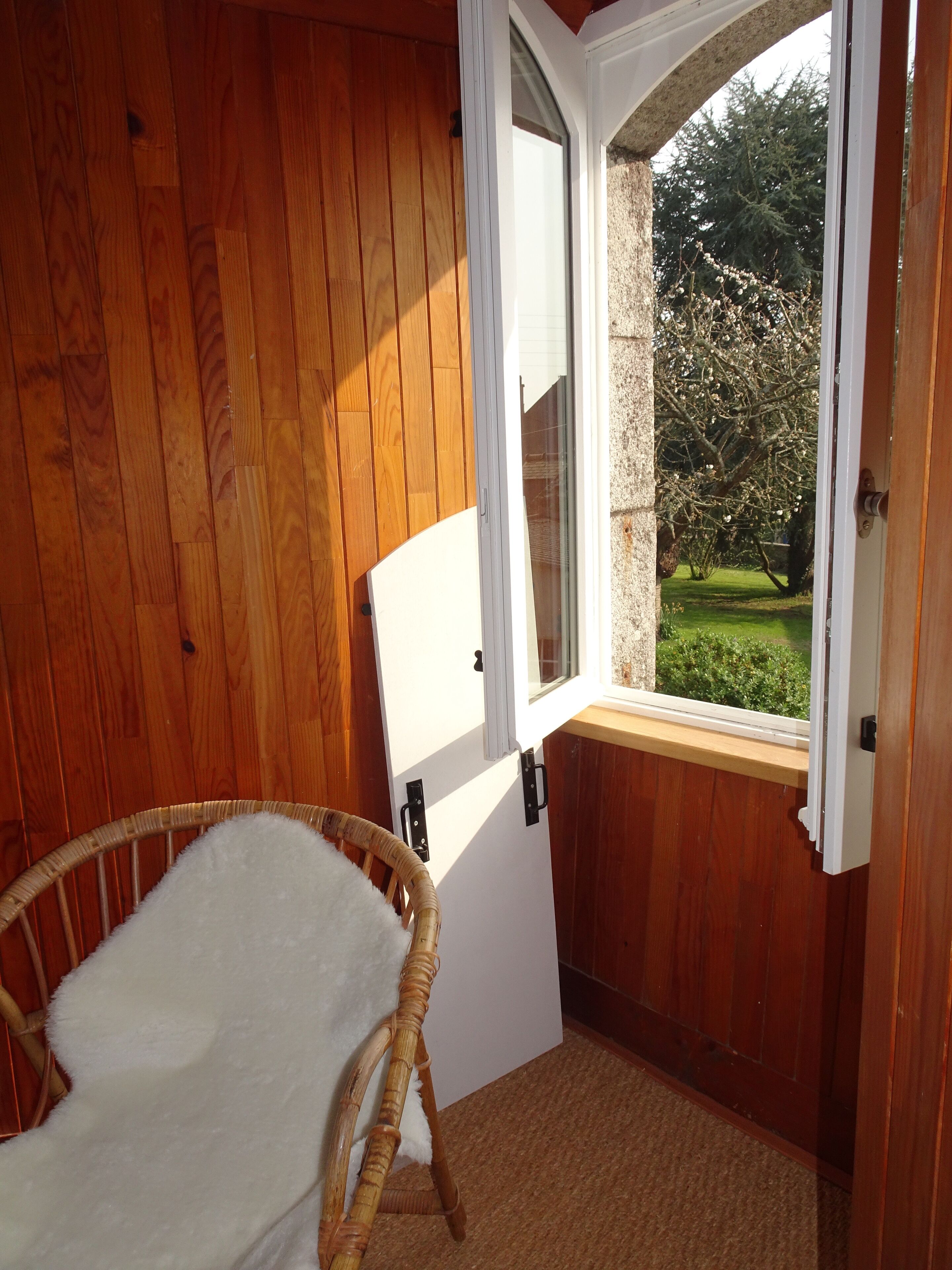 A wooden room with a wicker chair, a window with a view of a garden, and a white door.