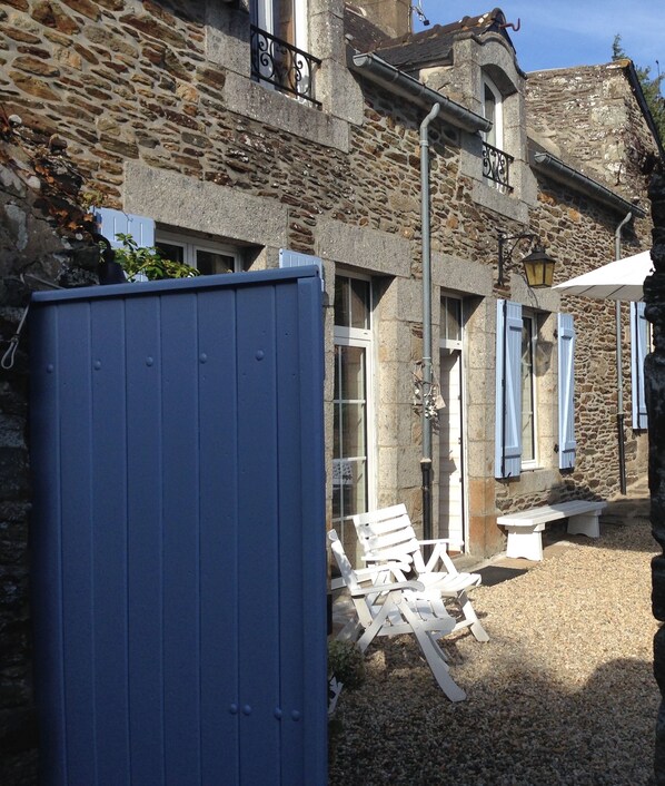 A stone building with a rustic exterior, a wooden door, and a small outdoor seating area with white chairs and a table.