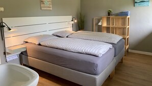 Un dormitorio moderno con cama, mesitas de noche, lámpara de noche, estante de madera con toallas y una planta en maceta.