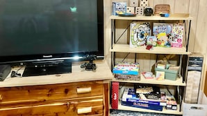 A room with a television, wooden drawers, and shelves with board games and puzzles. - Game Room, Fireplace and pit, very private, a little taste of heaven! (Dahlonega)