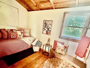A bedroom with a bed, pillows, a small table, a wall-mounted picture, and a window with blinds. - Game Room, Fireplace and pit, very private, a little taste of heaven! (Dahlonega)