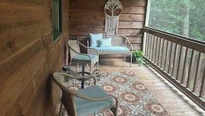 A wooden porch with wicker furniture, a patterned rug, and a macrame wall hanging. - Game Room, Fireplace and pit, very private, a little taste of heaven! (Dahlonega)