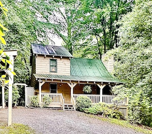 A wooden cabin with a porch, surrounded by greenery.