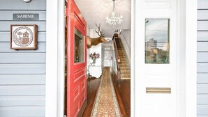 A hallway with a red door, a chandelier, and a staircase leading to another room. - Arbor House-Blue 1 (San Antonio)