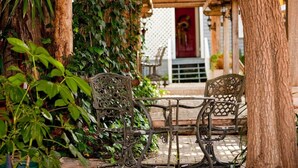 An outdoor seating area with wrought iron chairs and tables, surrounded by lush greenery and a wooden pergola. - Arbor House-Blue 1 (San Antonio)