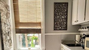 A compact kitchen with a window, a decorative wall piece, and a small trash bin. - Arbor House-Blue 1 (San Antonio)
