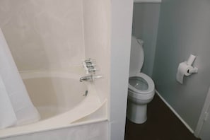 Un baño con bañera, inodoro y un dispensador de papel higiénico en la pared.