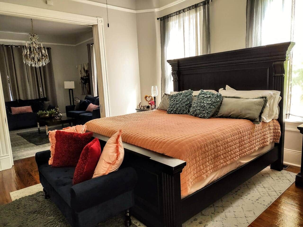 A bedroom with a large bed, a dark headboard, and a small seating area with a chair and ottoman.