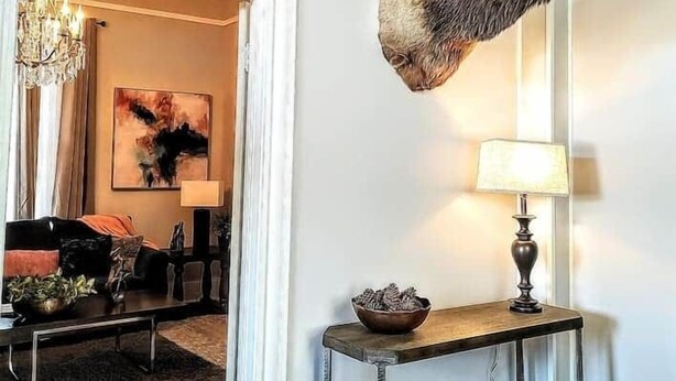 A room with a mounted deer head on the wall, a chandelier, a painting, and a console table with a lamp. - Arbor House-Blue 1 (San Antonio)