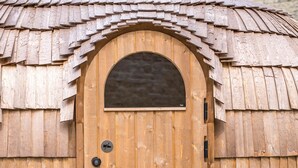 Une structure en bois dotée d’une grande porte en arc de cercle, d’une petite fenêtre et d’un banc à l’extérieur.