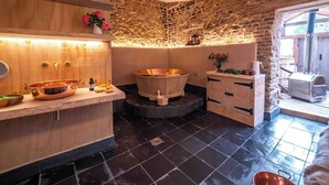 Une salle de spa avec un mur en pierre, des étagères en bois, une baignoire en cuivre et un meuble-lavabo en bois.