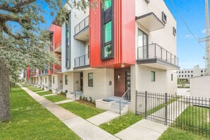 A modern apartment building with a brick facade, multiple balconies, and a well-maintained lawn.