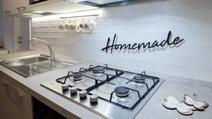 Une cuisine équipée d’une cuisinière à gaz, d’un évier en acier inoxydable et d’un pare-feu orné du mot « Fait maison ».