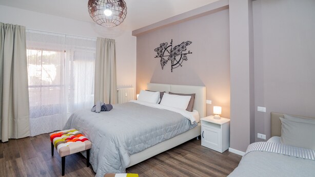 Une chambre à coucher moderne avec un grand lit, une table de chevet, une commode et un pouf coloré.