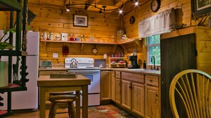 A wooden cabin kitchen with a stove, refrigerator, and wooden cabinets. - Cozy Cabin Among the Trees - Rustic Charm, Modern Comforts,  26 Secluded Acres  (Stoystown)