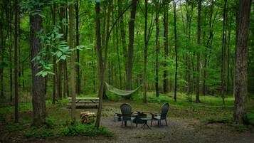 A forest campsite with a picnic table, two chairs, and a hammock.