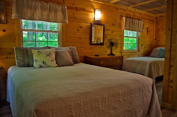Une chambre dans une cabane en bois, avec deux lits, une table de chevet, un miroir et une fenêtre donnant sur la forêt.