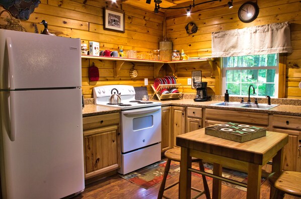 A wooden cabin kitchen with a refrigerator, stove, sink, and wooden table.