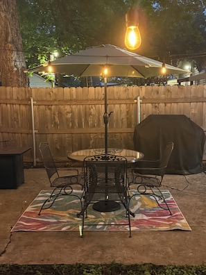 An outdoor patio with a round table, four chairs, a table lamp, and a barbecue grill. - Clay Cottage- Magnolia, Baylor and Downtown Waco (Waco)