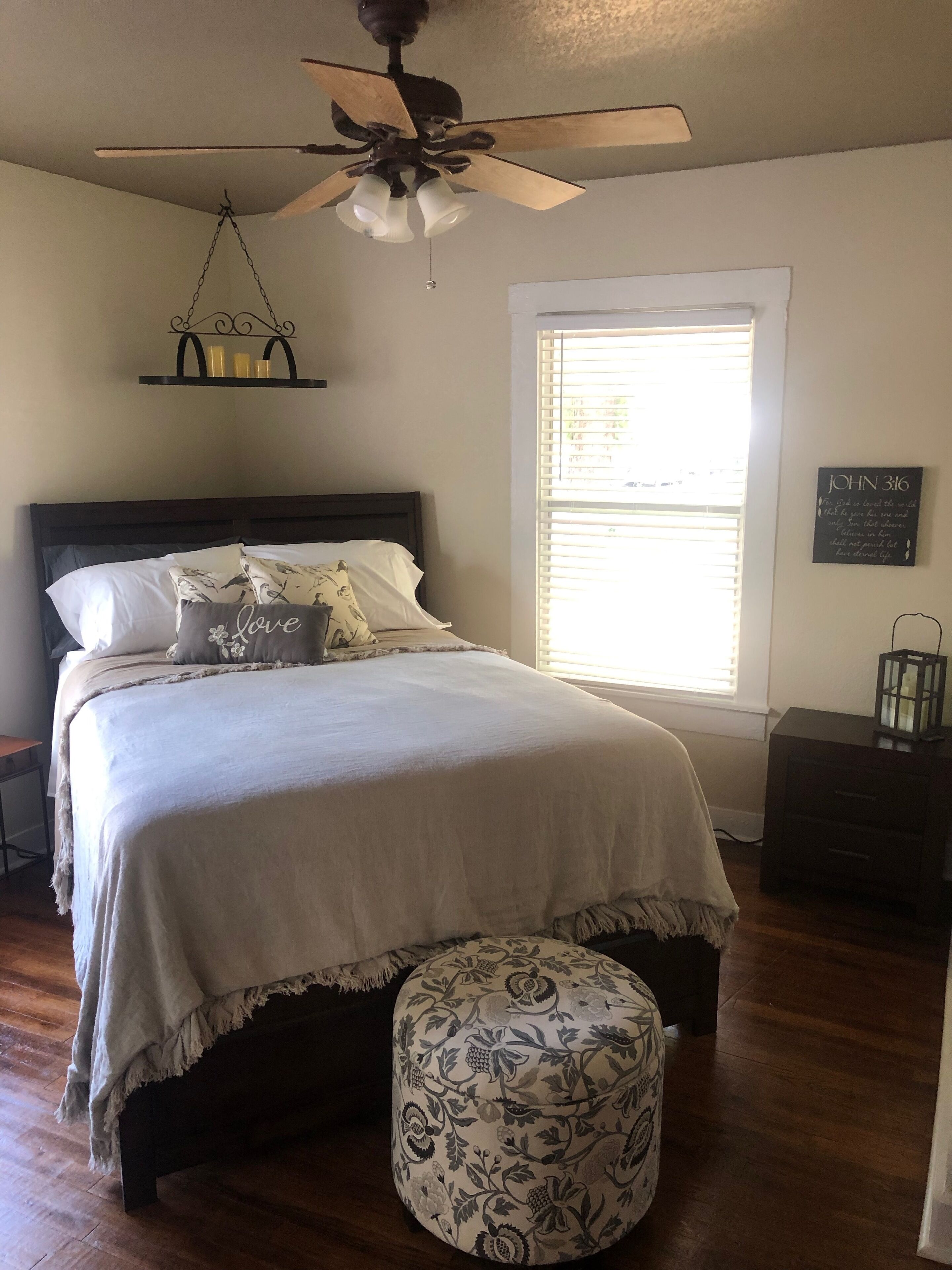 A bedroom with a bed, a ceiling fan, a window with blinds, a bedside table, and a nightstand.