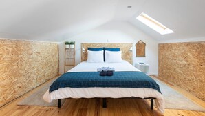 A bedroom with a sloped ceiling, a skylight, a bed with a blue and white checkered bedspread, and wooden walls. - The Tin Artist Atelier 1 bedroom apartment (Lisboa)
