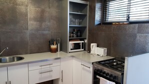 A modern kitchen with white cabinets, a stainless steel sink, a microwave, a toaster, and a gas stove. - Champagne views on a budget (Fremantle)