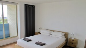 A bedroom with a bed, two bedside tables, a window with a curtain, and a view of a brick wall and greenery outside. - Champagne views on a budget (Fremantle)