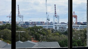 A view of a port with shipping containers and cranes, buildings in the background, and trees in the foreground. - Champagne views on a budget (Fremantle)