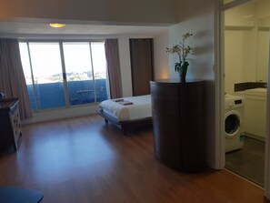 Une chambre d’hôtel avec un lit, un petit bureau, un lave-linge et une vue sur la ville grâce à de grandes fenêtres.