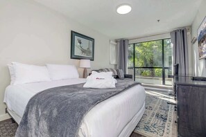 Une chambre d’hôtel avec un lit, un bureau, une chaise, une fenêtre avec des rideaux et un tableau au mur.
