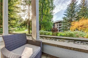 A balcony with wicker furniture, a view of a building, and surrounding greenery.