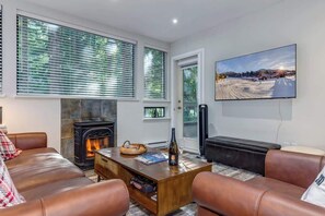A cozy living room with leather sofas, a fireplace, a coffee table, and a large TV screen displaying a snowy landscape.