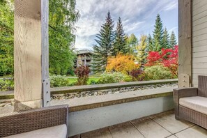 Un espace extérieur abrité offrant une vue sur une maison, un banc en pierre et une chaise en osier.