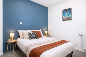 A bedroom with a bed, two bedside tables, a nightstand, a wall-mounted picture, and a radiator.