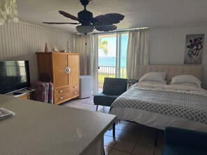 A hotel room with a bed, a television, a wooden cabinet, a chair, and a balcony with a view of the sea. - View Beachfront, Turtles, swim snorkel sun. AC Free parking Washer dryer. (Hauula)