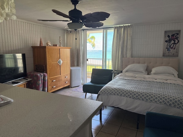 A hotel room with a bed, a television, a wooden cabinet, a chair, and a balcony with a view of the sea. - View Beachfront, Turtles, swim snorkel sun. AC Free parking Washer dryer. (Hauula)