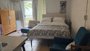 Een slaapkamer met een bed, een bureau, een stoel, een kledingkast, een plafondventilator en een raam met gordijnen.