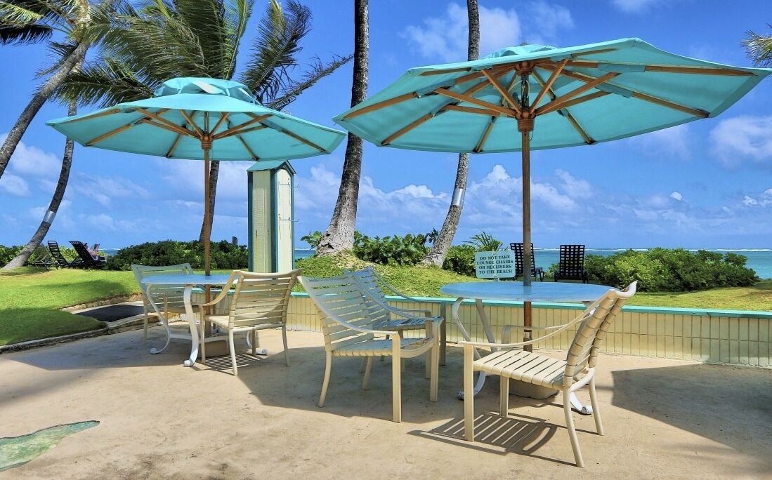 A poolside area with two umbrellas, lounge chairs, and a view of the ocean.