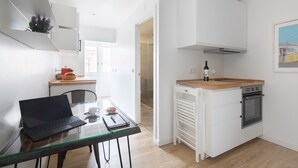 A compact kitchen with a small dining area, a laptop on the table, and a bottle of wine. - The Iron Artist Studio Atelier (Lisboa)