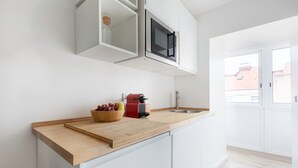 A modern kitchen with white cabinetry, a wooden countertop, a red coffee maker, and a bowl of fruit. - The Iron Artist Studio Atelier (Lisboa)