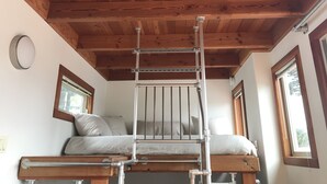 Un dormitori d'estil loft amb sostre de fusta, escala metàl·lica, lliteres i una finestra.