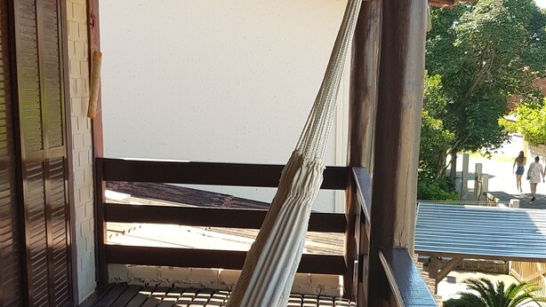 A hammock under a wooden structure with a view of a building and a tree. - Casa do Sassá - Close to everything (Guarda do Embaú)