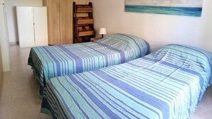 Et værelse med to senge, et træskab, et lille bord med en lampe og et maleri af en strand.
