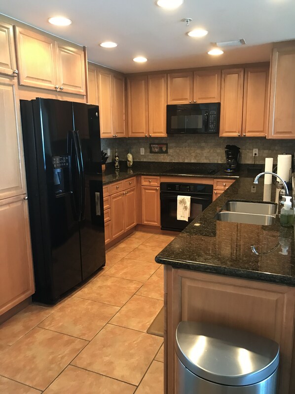 Una cocina moderna con armarios de madera, un refrigerador negro, un microondas y un lavamanos de acero inoxidable.