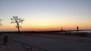 A beach scene with a bench, a tree, and a lighthouse in the background. - House steps from the beach. (Pentwater)